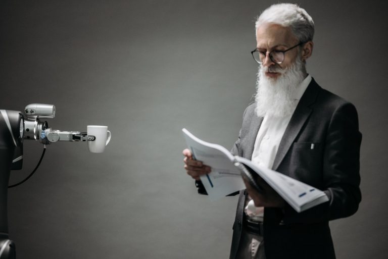 A robot arm assists a professional with a book and coffee in a modern office setup. Technology meets innovation.
