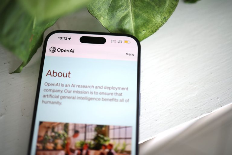 Close-up shot of a smartphone screen showing the OpenAI website with greenery in the background.