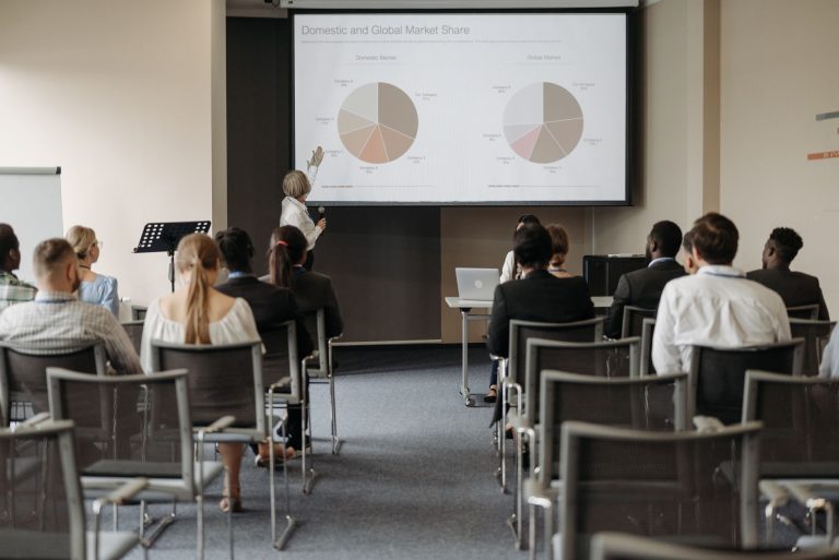 Business conference with diverse audience and speaker presenting market data.