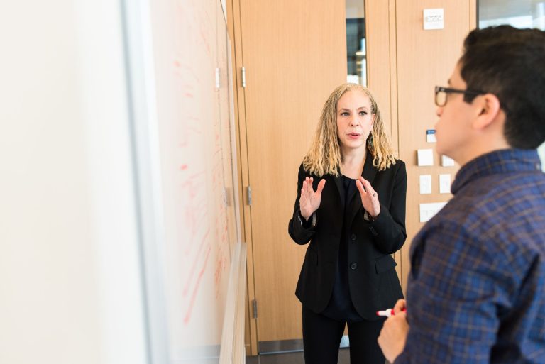 Two professionals discussing ideas at a workplace whiteboard. Collaborative team meeting.